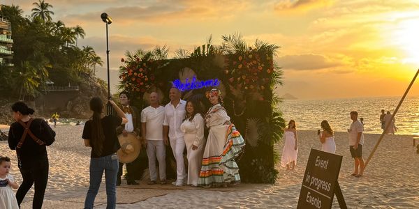 Group posing for photos at a beach event during sunset.