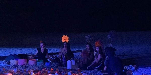 Group of people gathered around a fire at night with decorative flower crowns.
