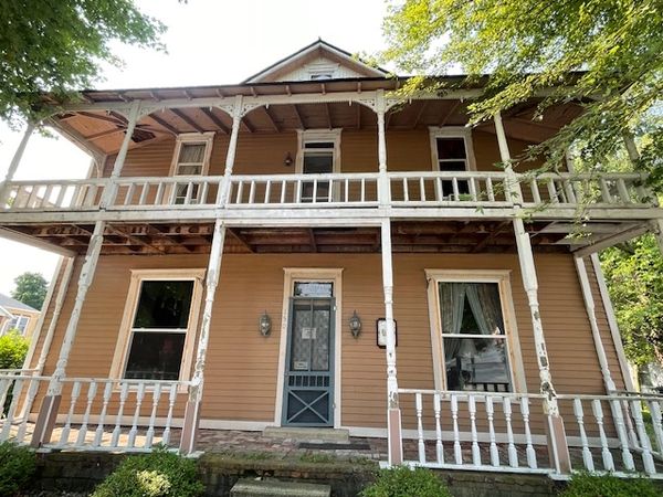 Old two-story house with a weathered white porch and brown exterior.