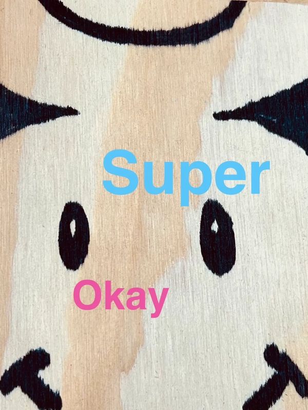 Close-up of a painted cow face on wood with 'Super' and 'Okay' text.