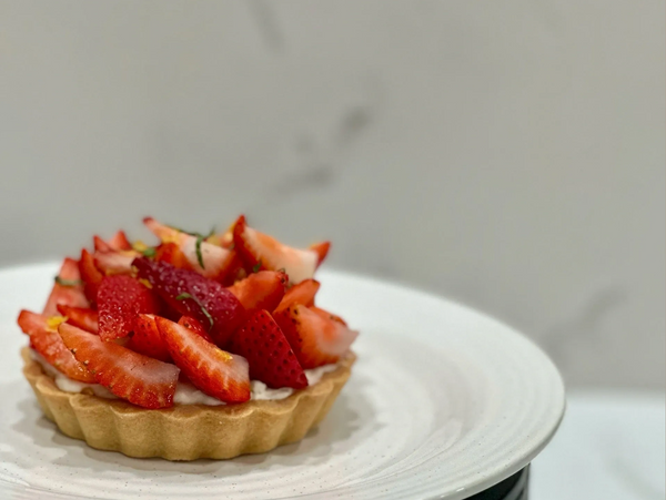 Strawberry tart with fresh slices on a white plate.