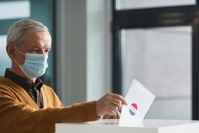 An elderly man wearing a mask casts his vote with a ballot.
