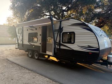 Modern travel trailer parked on a pathway under trees.