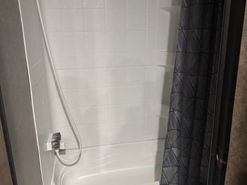 Clean white bathtub with gray shower curtain.