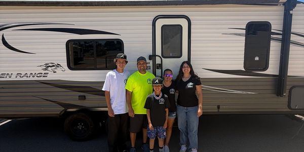 Family posing in front of a caravan on a sunny day.