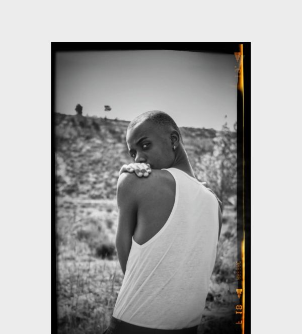 Black and white portrait of a person in a white tank top looking over their shoulder outdoors.