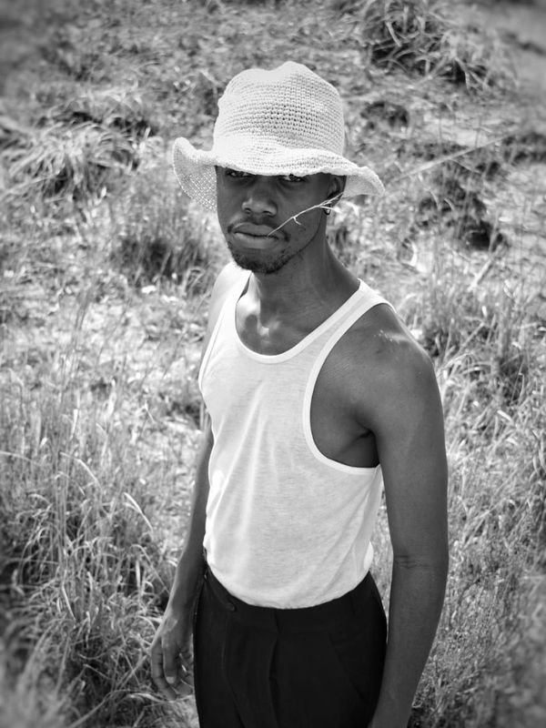 Man in a white tank top and hat standing in a grassy field.