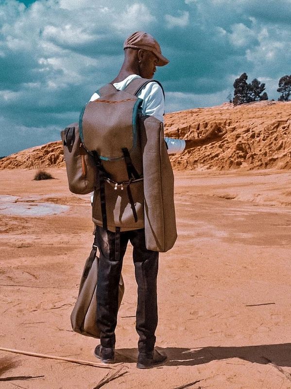 Person wearing multiple large backpacks standing in a desert landscape.
