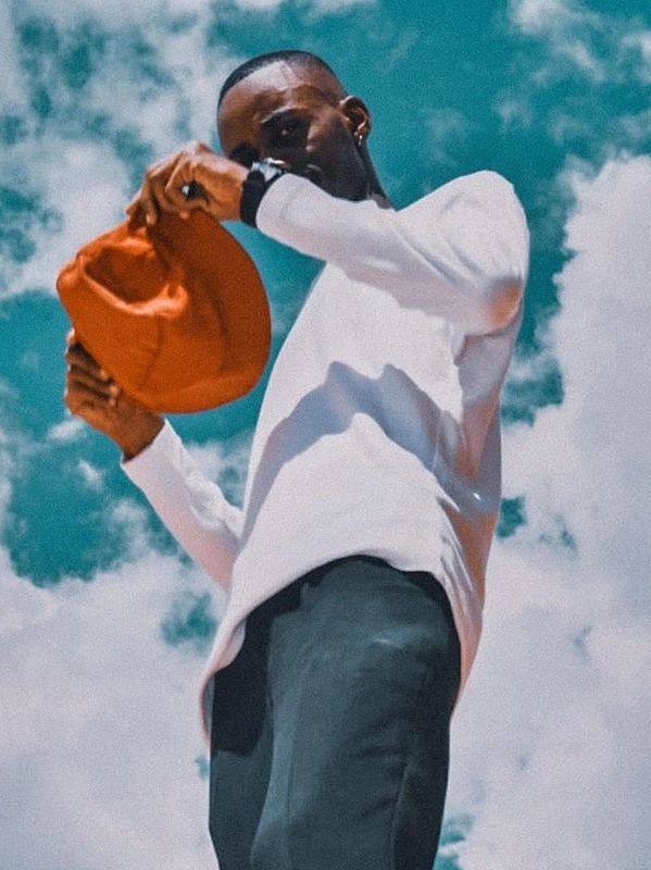 Man in white shirt holding an orange hat against a blue sky.