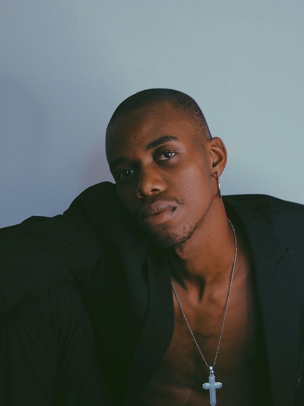 Pensive man with a cross necklace and earring in a dark blazer.