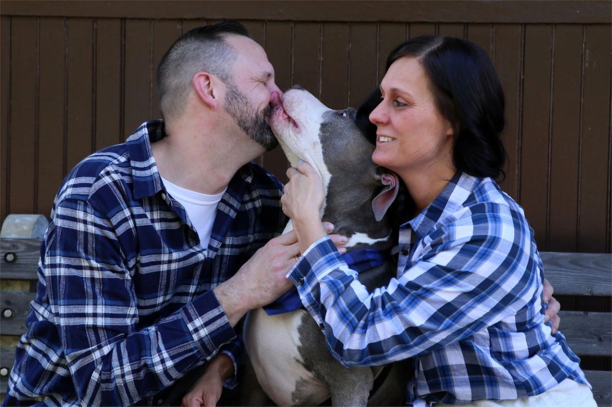 A heartwarming scan allaire state park engagement photo shoot, capturing a joyful dog playfully licking its owner's face while the couple laughs in delight. The candid moment embodies love, happiness, and the playful spirit of the couple's relationship.