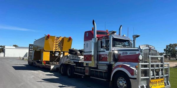 Large semi-truck hauling an oversized yellow industrial machine on a flatbed trailer.