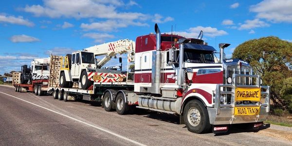 Large red and white truck hauling heavy machinery on a flatbed trailer.