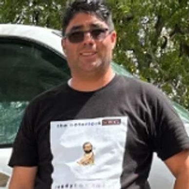 Man wearing sunglasses and a black graphic t-shirt outdoors.