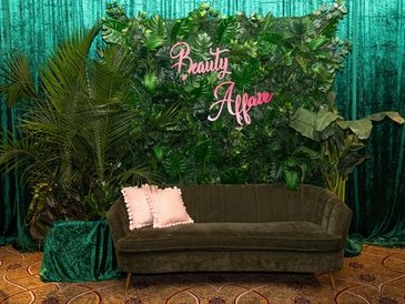 Elegant green velvet sofa with pink pillows against a lush leafy backdrop.