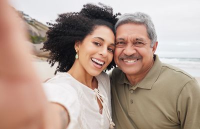 A woman and an older man smiling and taking a selfie on the beach.