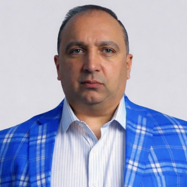 Man in a blue plaid blazer and white striped shirt against a plain background.