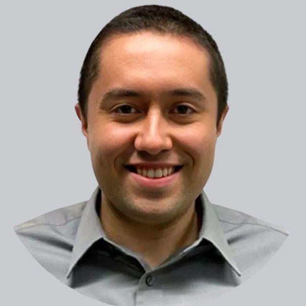 Smiling man in a gray shirt against a plain background.