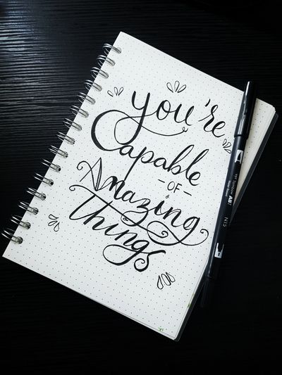 A note pad and pen on a table with"Your capable of amazing things" written on it.