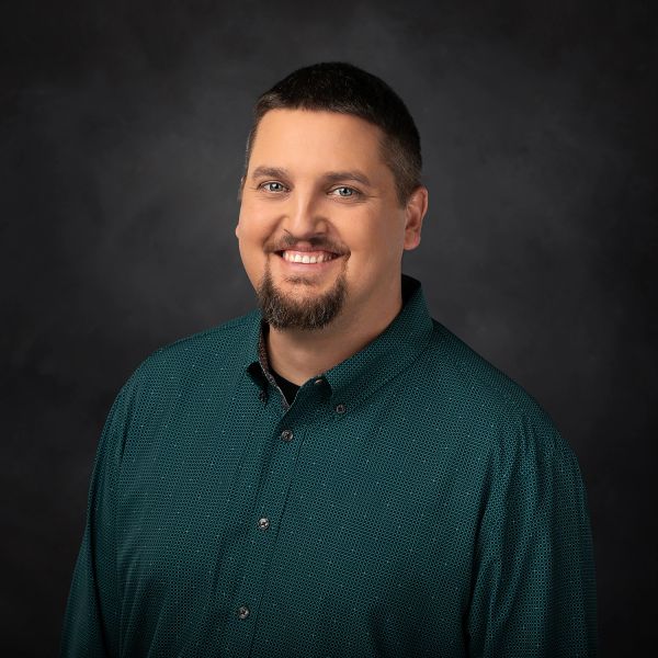 Smiling man in a green shirt against a dark background.