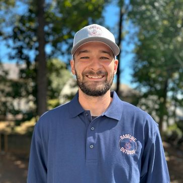 Smiling man wearing a blue polo and gray cap outdoors.