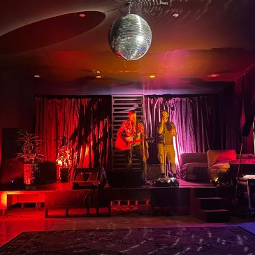 Two performers on stage under a disco ball in a dimly lit venue.