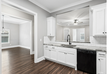 Modern white kitchen with dark wood floors and black appliances.