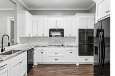 Modern white kitchen with black appliances and wood floors.