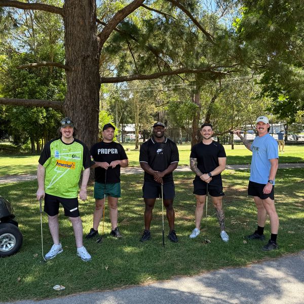 Five men posing with golf clubs on a sunny day in a park.