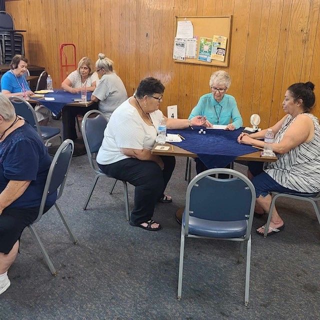 A group of elderly women playing a tabletop game in a community room.