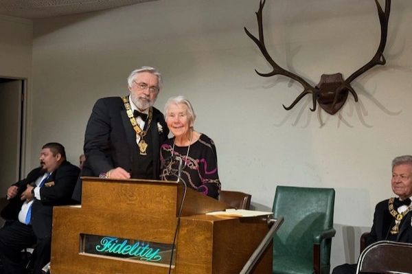 Two elderly people pose behind a wooden podium with antlers on the wall.
