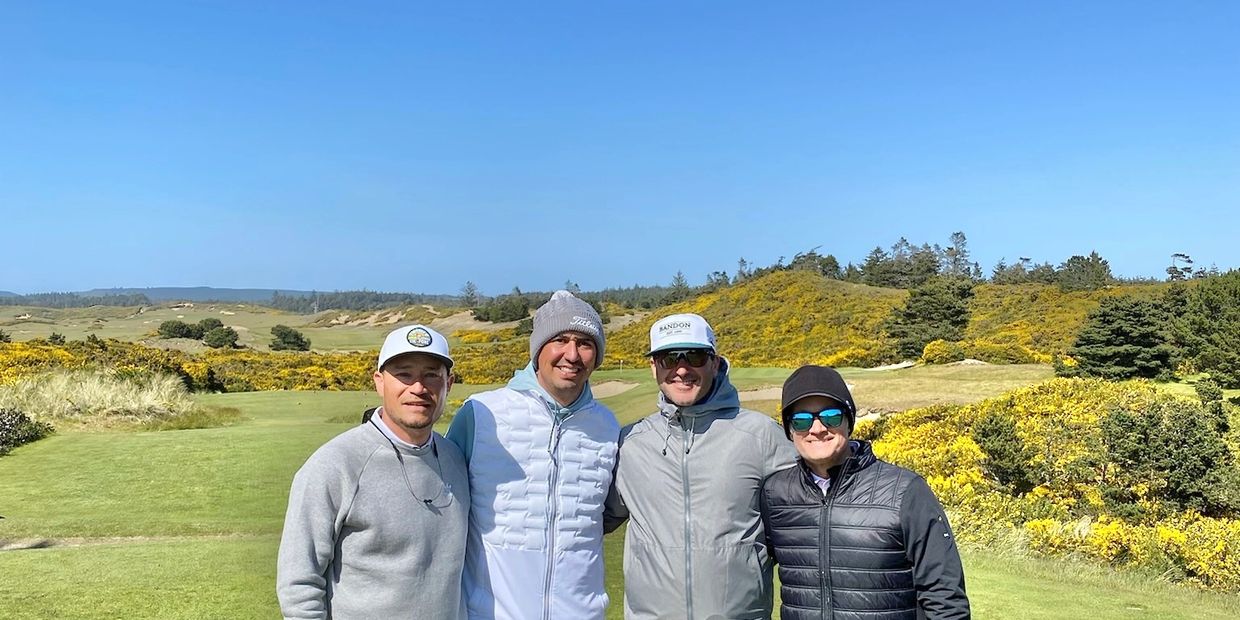 Four men posing on a sunny golf course with clear blue skies.