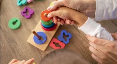 Adult guiding child to stack colorful wooden rings on a peg toy.