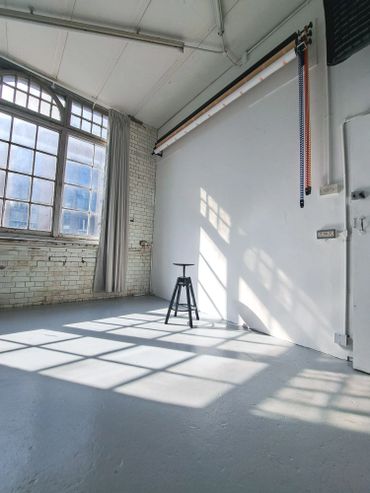 Bright, empty studio space with large windows and a single stool.