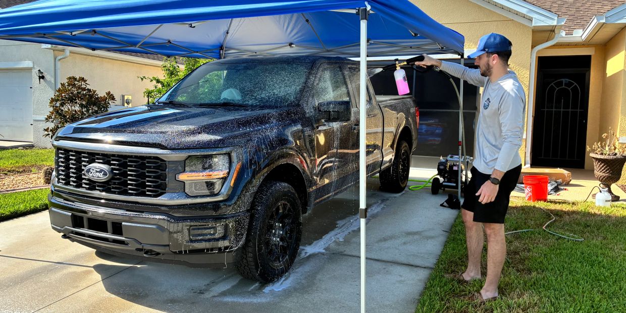 A man washing a black truck under a canopy.
