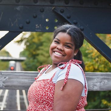 Smiling woman in red dress standing on a wooden bridge.
