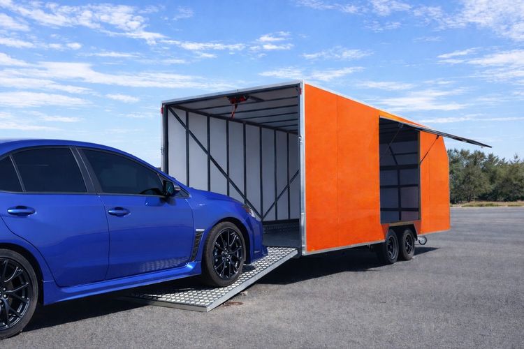 Blue car driving up a ramp into an orange enclosed trailer.
