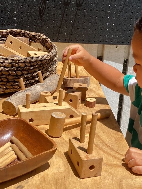 Child playing with wooden blocks and pegs on a table in sunlight.