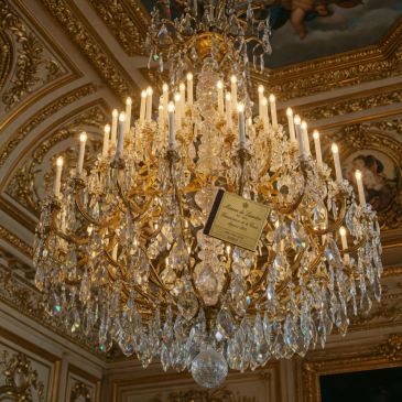 Luxurious crystal chandelier with lit candles in an ornate room.