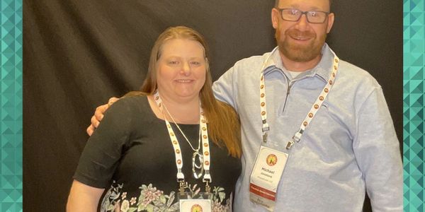 Two people smiling with conference badges around their necks.