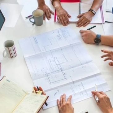 People collaborating over architectural plans at a table with notebooks and coffee.