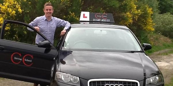 Man standing by a black driving school car with an L-plate on top.