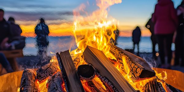 A close up of a bonfire on the beach with blurred figures in the distance