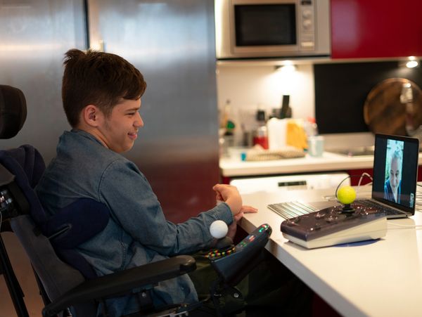 A young disabled man sits in the kitchen on a video call