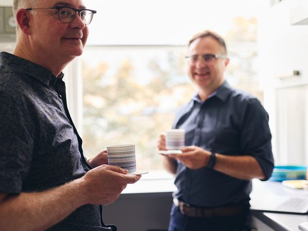 Two men chatting in a kitchen holding coffee cups