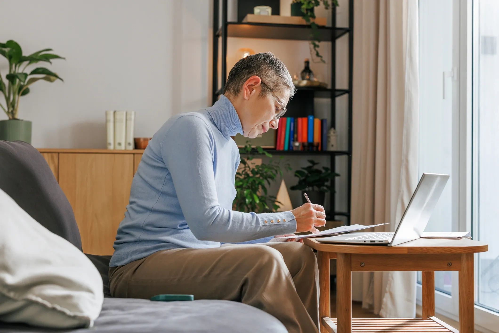 A woman working on papers with a laptop nearby.