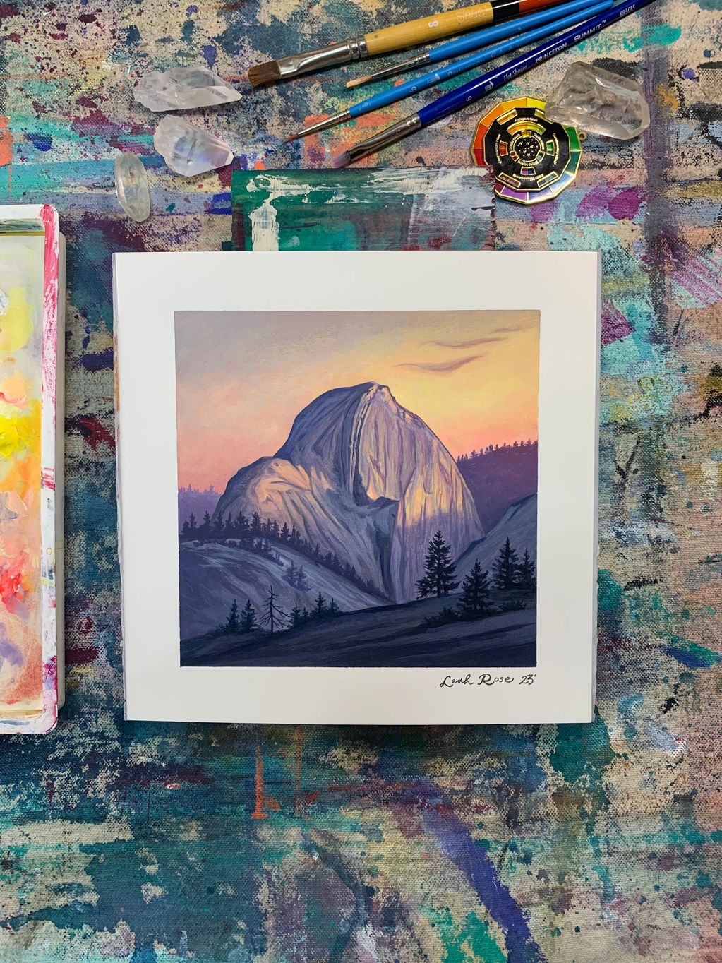 A mountain painting with brushes and crystals on a colorful surface.
