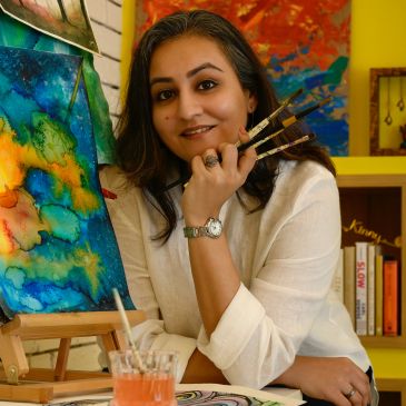 Woman artist holding paintbrushes with colorful paintings in background.