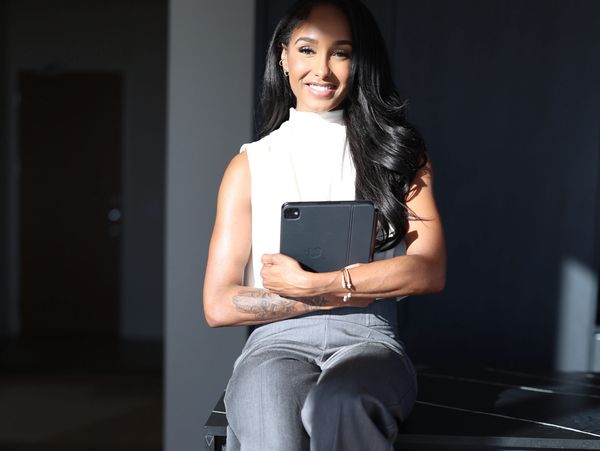 Confident woman sitting on a table holding a tablet, smiling warmly.