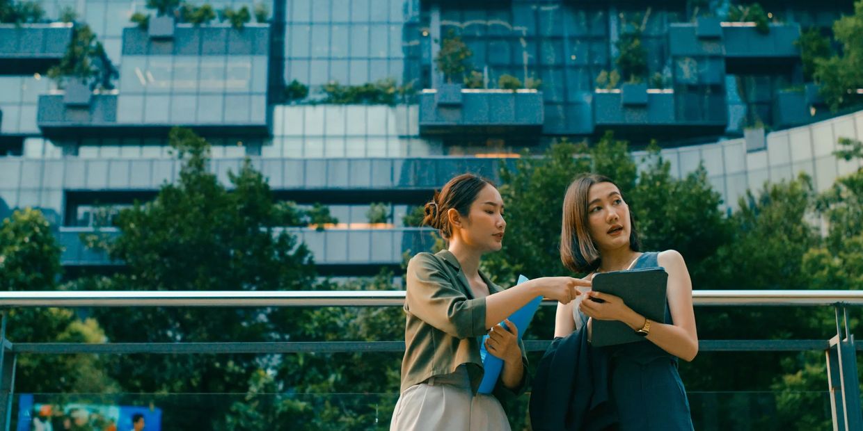 Two women discussing documents outdoors in front of a modern building.
